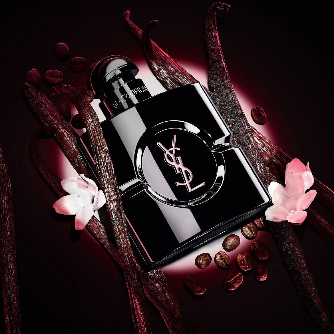 Black Opium Le Parfum Flakon in glanzendem Schwarz, umgeben von dunklen Vanilleschoten und weißem Jasmin.
