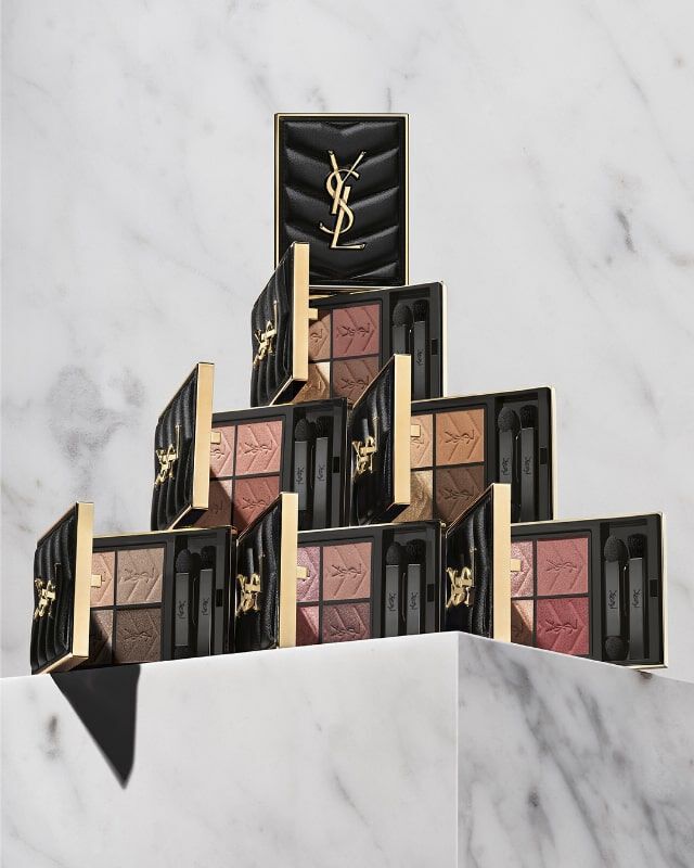 A stylish display of Yves Saint Laurent makeup palettes stacked in a pyramid formation on a marble surface, with a sleek black case at the top.