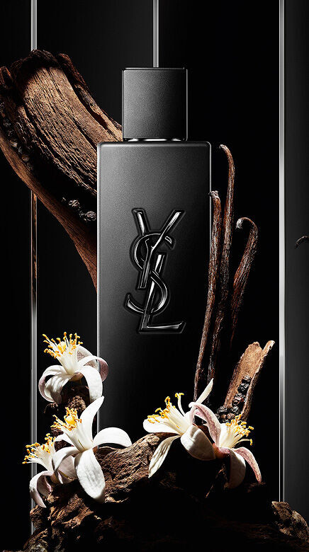 Schwarzer YSL-Parfumflakon, umgeben von Holz, Vanilleschoten und weißen Bluten.