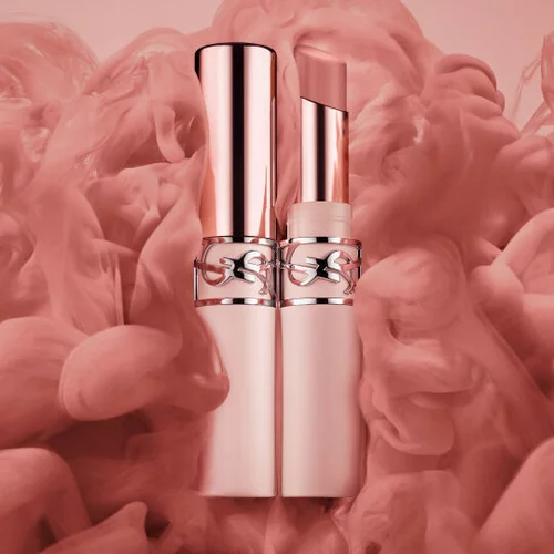 Zwei rosegoldene Lippenstifte vor einem weich-rauchigen rosa Hintergrund.