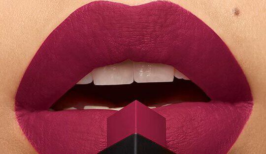 Close-up of lips painted in a deep burgundy shade, with a lipstick bullet positioned at the center. The texture appears smooth and matte.