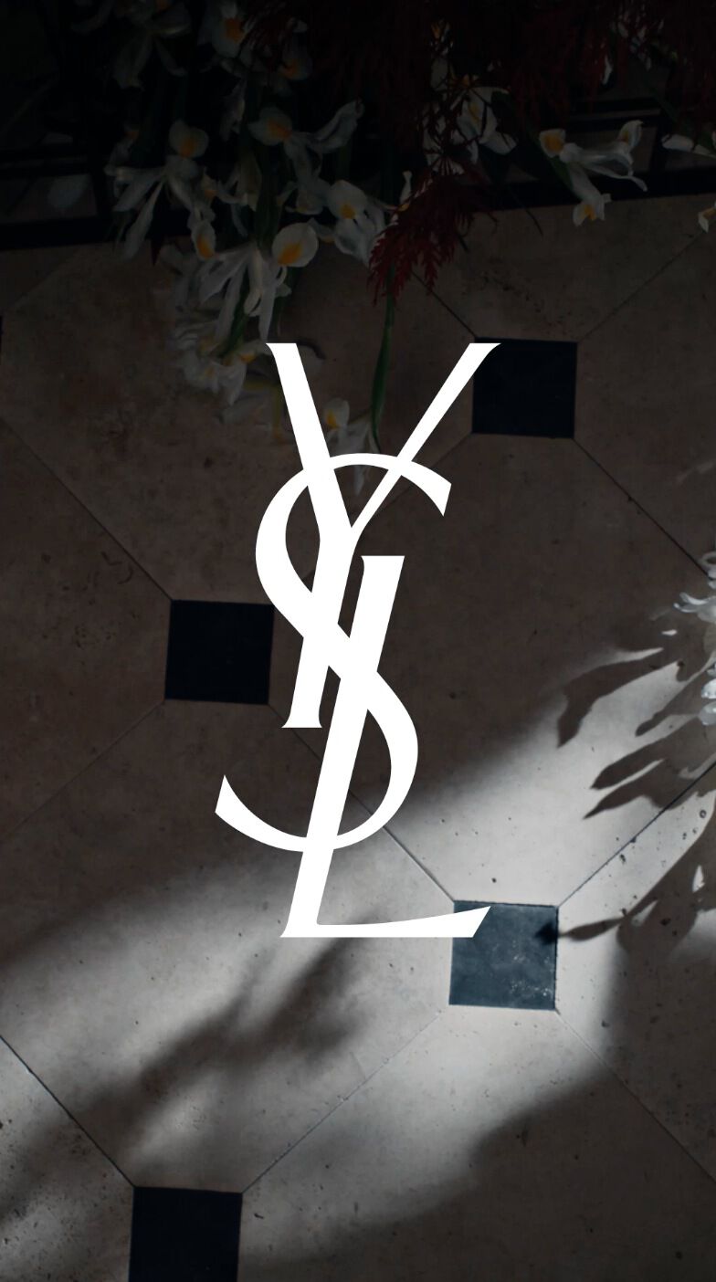 A stylish logo of "YSL" is displayed on a patterned floor, surrounded by shadows and delicate white flowers.