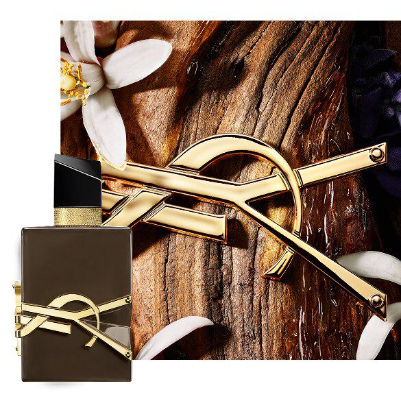 Libre Santal Couture braune, glasierte Flakon auf Sandelholzrinde mit goldener Cassandre und weißen Bluten.