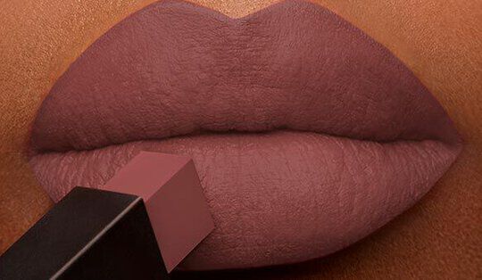 Close-up of a pair of full lips being applied with a matte lipstick in a soft mauve shade.