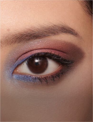 Close-up of an eye featuring a makeup look with shades of brown, pink, and blue, highlighting the eyelashes and brow.
