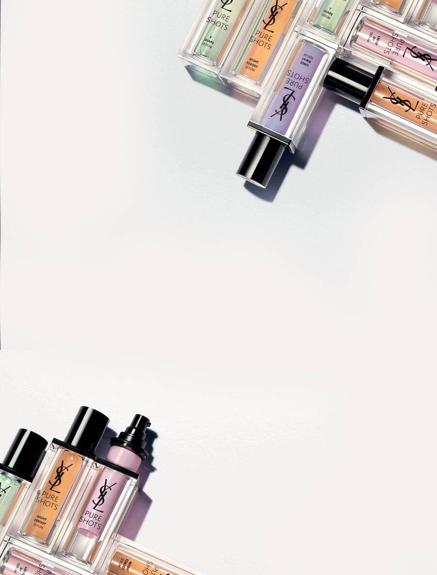 A flat lay of various YSL beauty products, including bottles of foundation and other makeup items, arranged artistically on a light background.