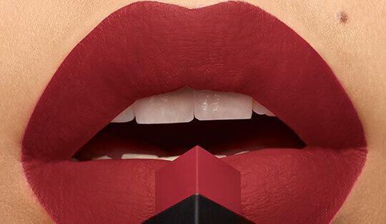 Close-up of bold, red lips with a matte finish, partially open, showcasing a lipstick bullet positioned at the center.