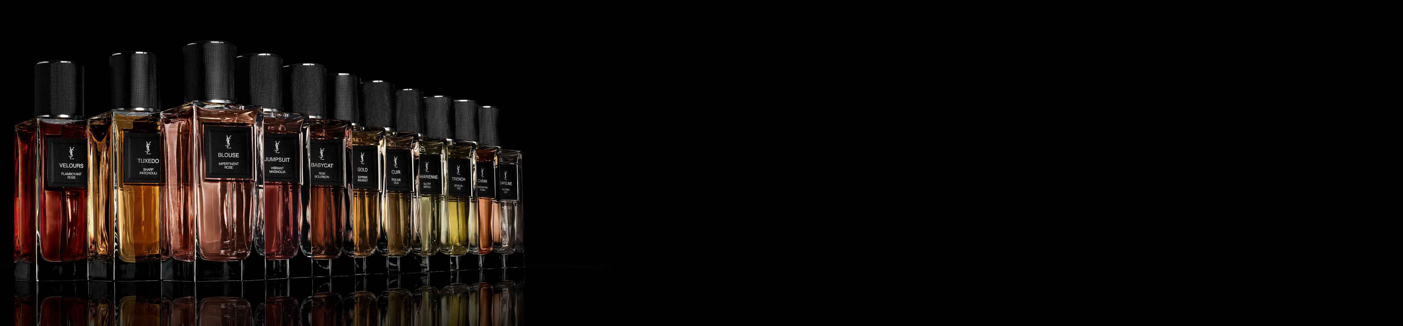Eine Reihe von Yves Saint Laurent Parfumflaschen mit Flussigkeiten in verschiedenen Farben und schwarzen strukturierten Kappen, die sich auf einer dunklen Oberflache vor schwarzem Hintergrund spiegeln.