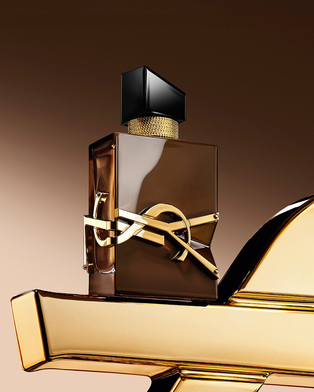 Glasierte braune Libre Santal Couture Flasche, die Licht reflektiert, auf einer großen goldenen YSL Cassandre platziert.