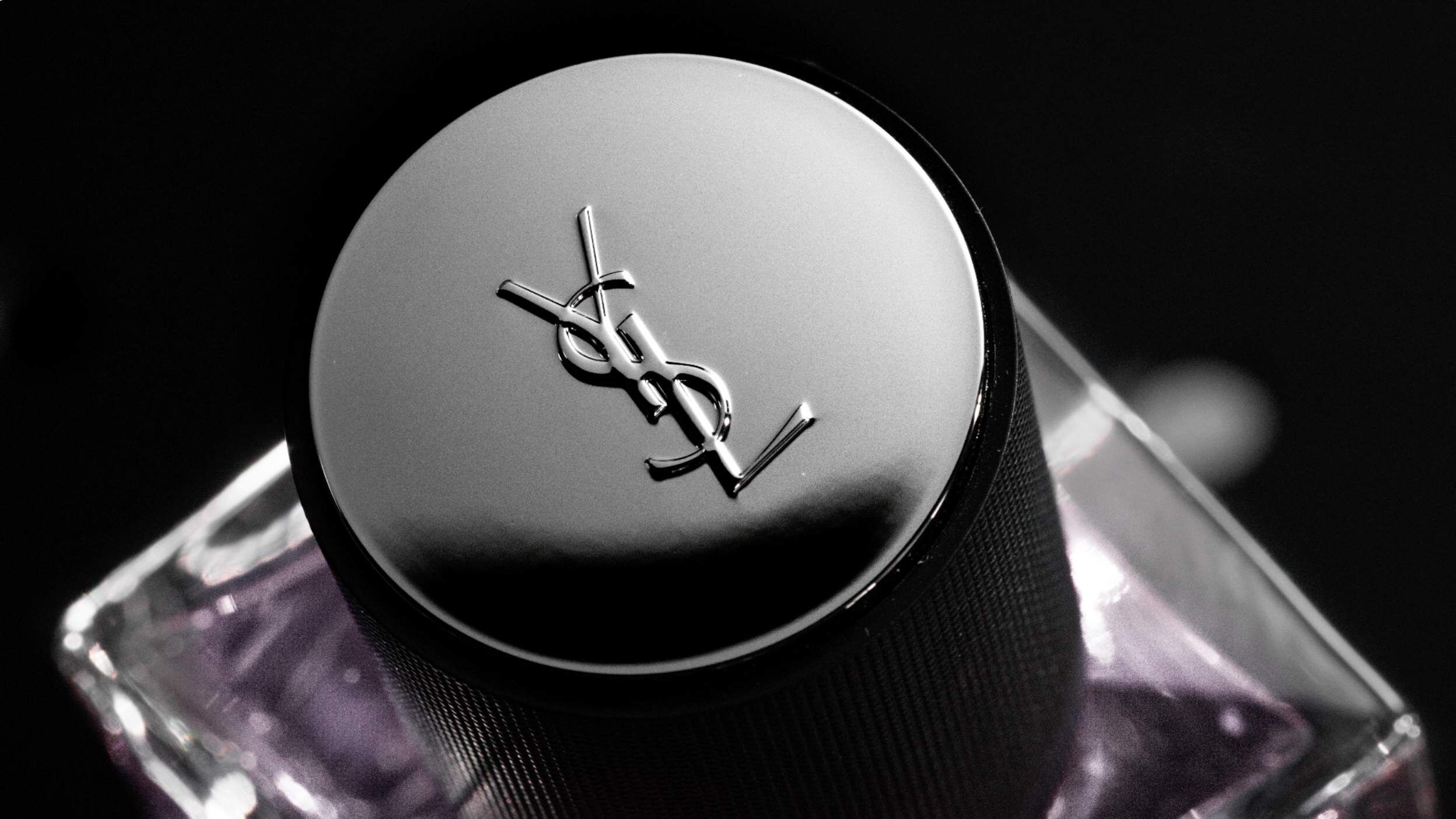 A close-up of a black and silver bottle cap with the YSL logo, featuring a glossy finish against a blurred background.