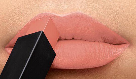 Close-up of a pair of lips with a nude lipstick being applied from a square tube.