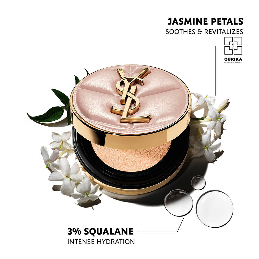 Pinkfarbene, gesteppt YSL SKIN AFFAIR CUSHION FOUNDATION mit goldenem Logo, umgeben von weißem Jasmin und Wassertropfen. Text betont Jasminbluten, Ourika Community Gardens und 3 % Squalan fur intensive Feuchtigkeit.