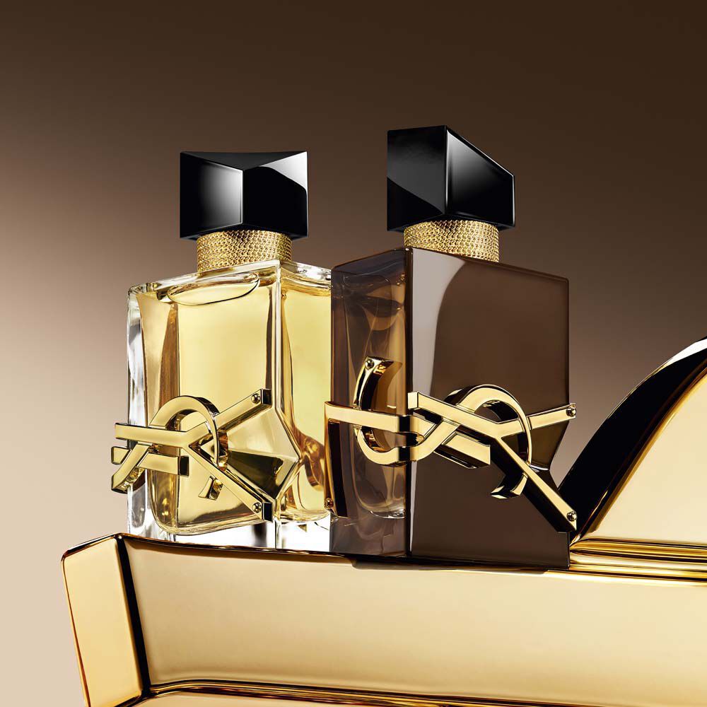 Glasierte braune Flakons von Libre Santal Couture und Libre Eau de Parfum, die das Licht reflektieren, auf einer großen goldenen YSL Cassandre platziert.