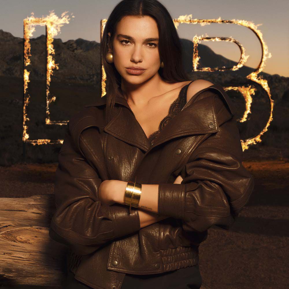 Dua Lipa in einer braunen Lederjacke vor großen, lodernden LIBRE Lettern in einer rauen Wustenlandschaft.