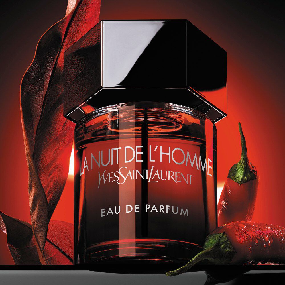 The La Nuit de l’Homme Eau de Parfum bottle paired with a red chili pepper and a dry leaf, representing its spicy and incandescent scent.