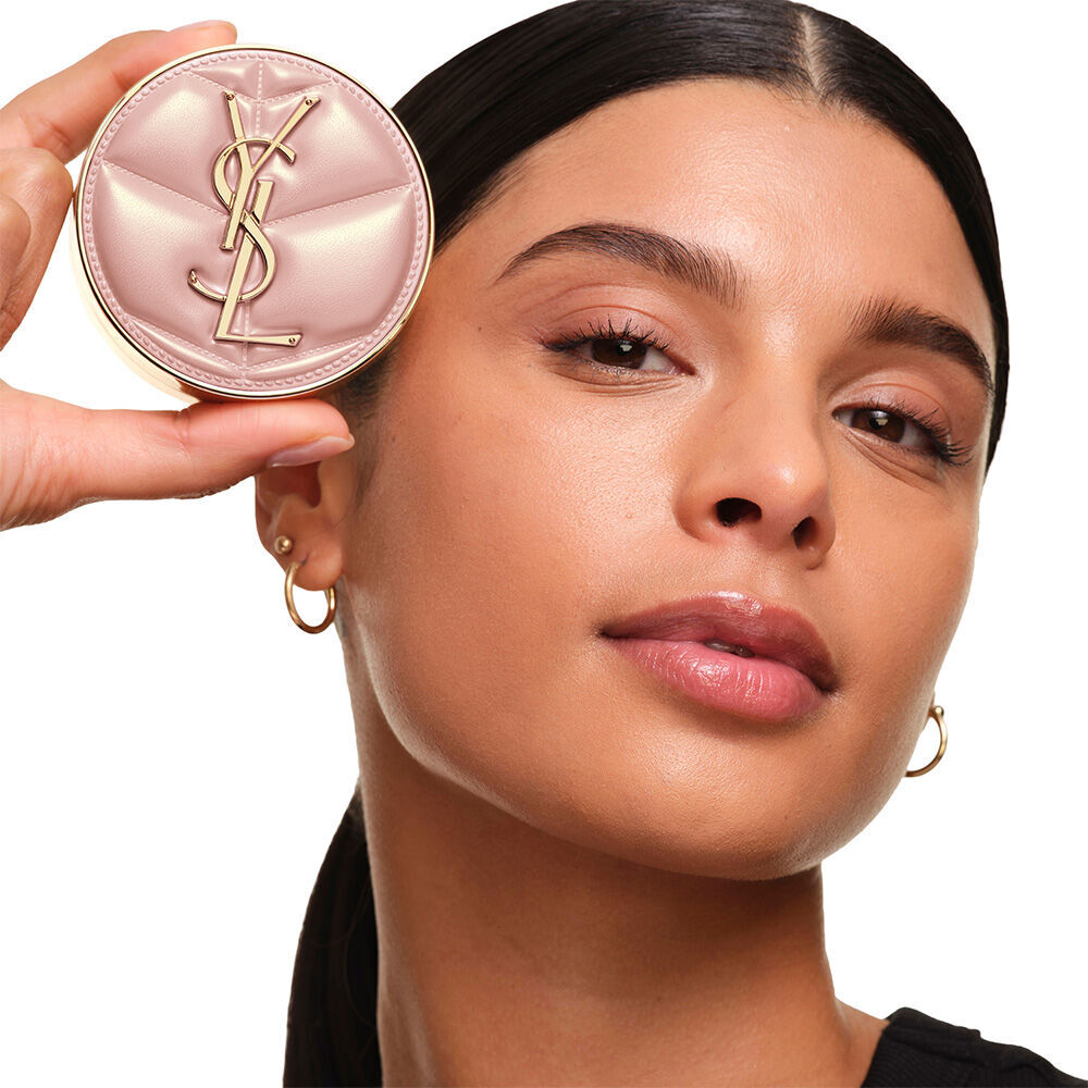 Das Model mit glatter, strahlender Haut halt das pinke YSL SKIN AFFAIR CUSHION FOUNDATION, um ein naturlich leuchtendes, makelloses Hautfinish zu prasentieren.