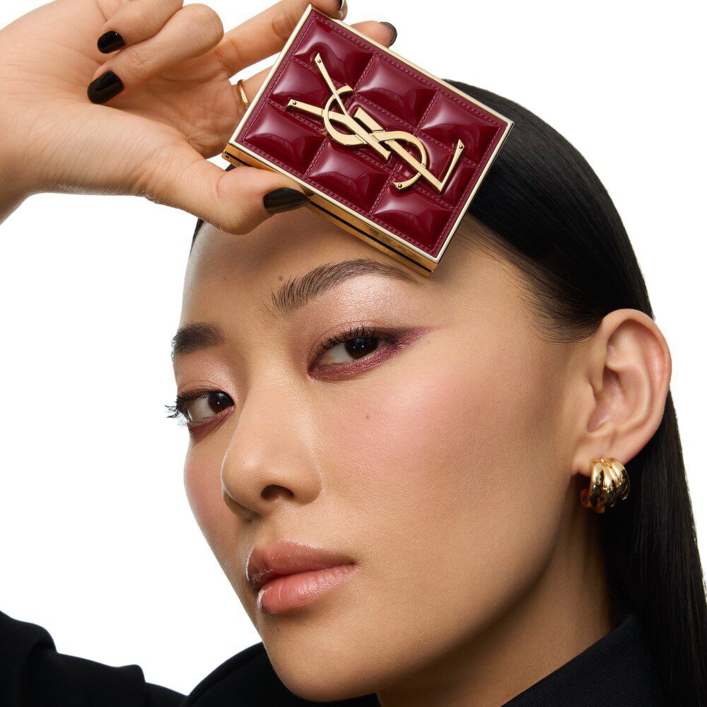Model in schwarzem Anzug und glamourosem Look, thront in festlichem Kerzenlicht zwischen YSL-Geschenkboxen.