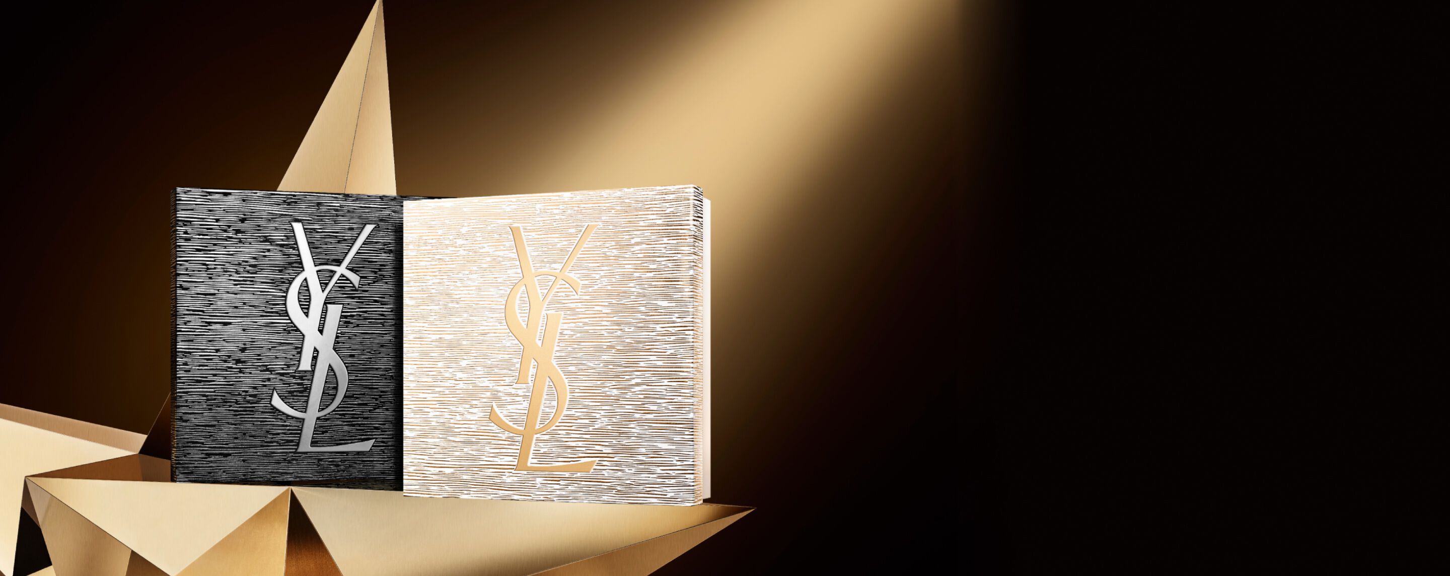 Zwei elegante YSL Beauté-Geschenksets für die Feiertage, eines in Schwarz mit silbernem Logo und eines in Gold mit goldenem Logo, platziert auf einer geometrischen goldenen Oberfläche, die auf Couture und Brillanz hindeutet.