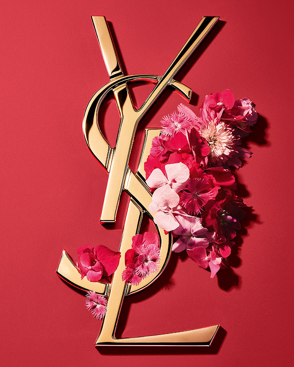 Goldenes YSL Cassandre-Logo, geschmückt mit leuchtend rosafarbenen Frühlingsblumen, auf einem rosafarbenen Hintergrund.