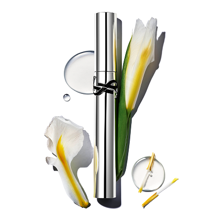 YSL LASH LATEX WIMPERNTUSCHE, EINE SCHLANKE SILBERNE TUBE, ELEGANT PRÄSENTIERT MIT WEISSEN UND GELBEN IRISBLÜTEN UND GLITZERNDEN FLÜSSIGKEITSTROPFEN.