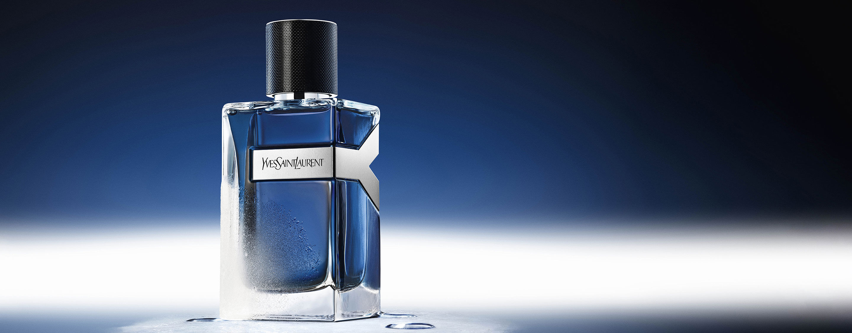 YSL Y Eau de Toilette Intense Iced Cologne 100ml Flakon, gefrostet und mit Wassertropfen bedeckt, spiegelt ein kühl-blaues Ambiente wider.