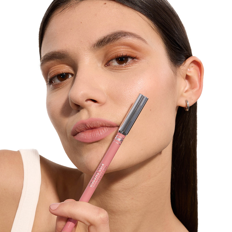 Nahaufnahme eines Models mit zartrosa matt geschminkten Lippen, das einen passenden YSL Kiss Shaper Lippenkonturenstift hält.