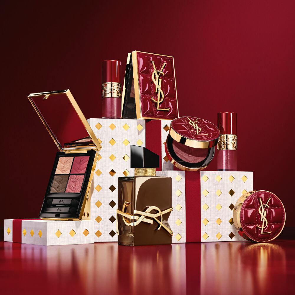 YSL Holiday 2026 Make-up-Kollektion und Duftset auf goldgepunkteten weißen Sockeln in Bordeauxrot.