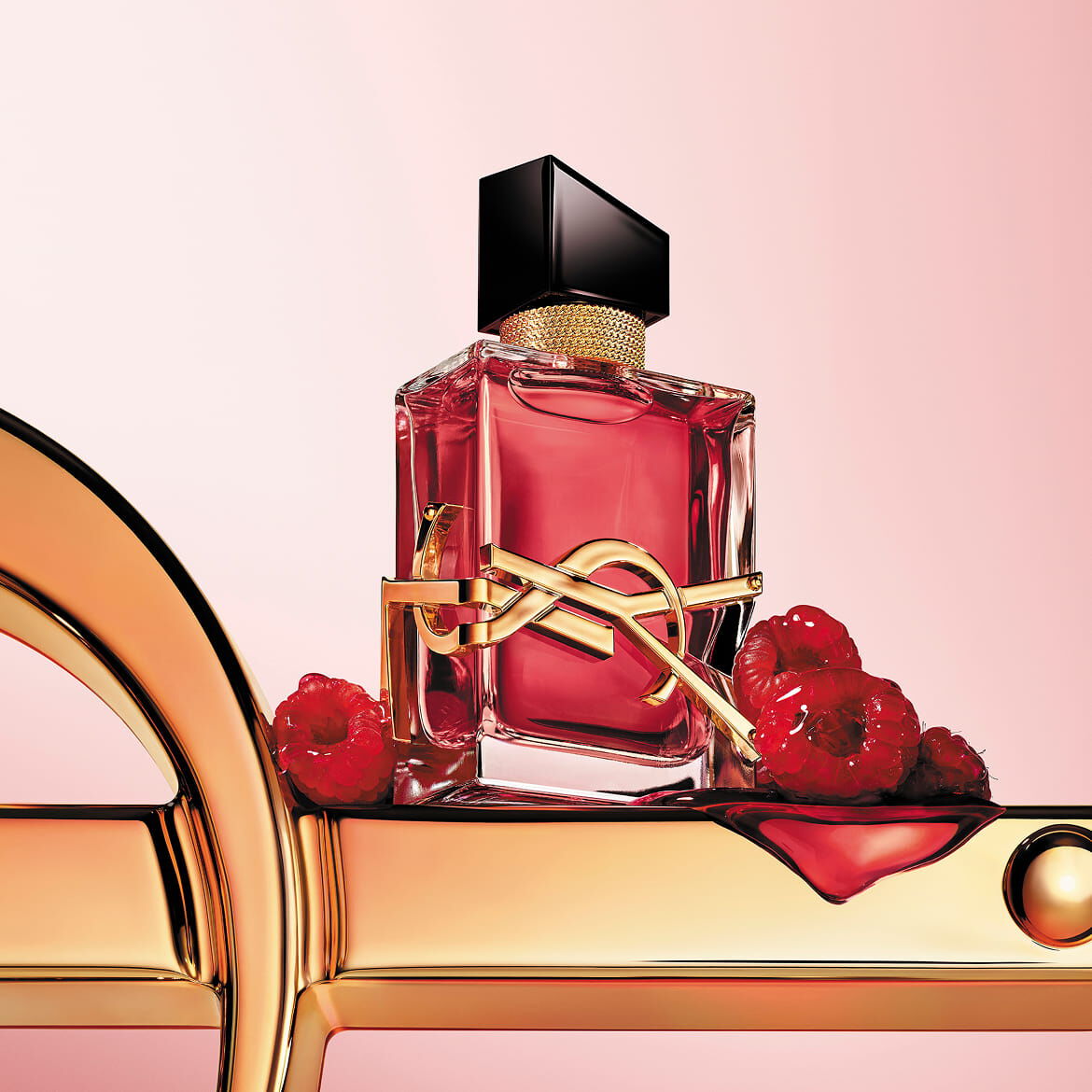 Roter YSL-Parfümflakon mit goldenem Logo auf einer goldenen Oberfläche mit Himbeeren.