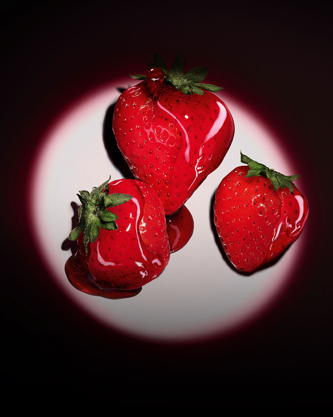 Drei frische rote Erdbeeren beleuchtet von einem pinken, kreisförmigen Spotlight auf dunklem Hintergrund.