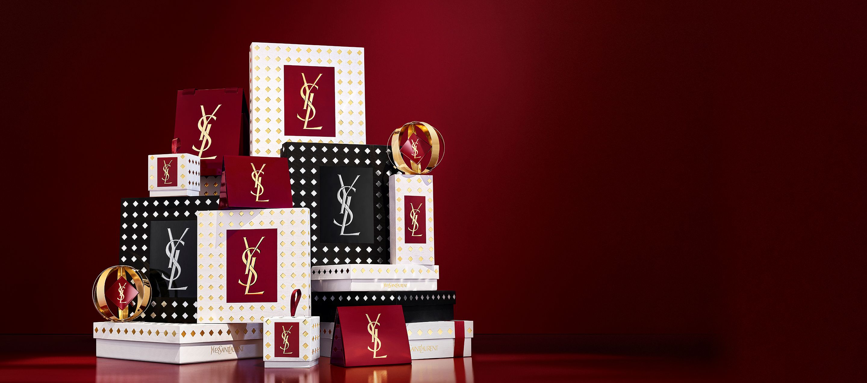 Drei Models in eleganten schwarzen Outfits halten YSL-Geschenksets vor einem festlichen roten Vorhang mit fallendem goldenem Konfetti.