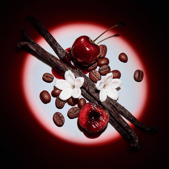 Nahaufnahme saftiger roter Kirschen, Jasminblüten, Vanilleschoten und Kaffeebohnen, dramatisch inszeniert im Spotlight für Black Opium Eau de Parfum Over Red.