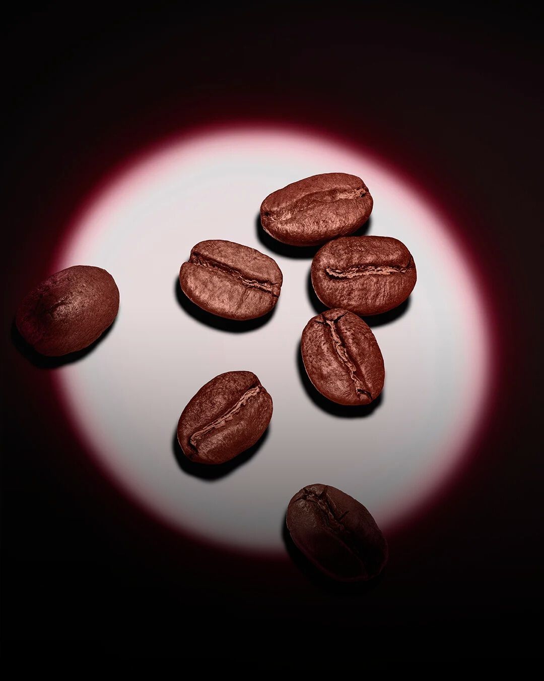Eine Gruppe gerösteter Kaffeebohnen, akzentuiert durch einen rosafarbenen kreisförmigen Lichtschein auf dunklem Hintergrund.