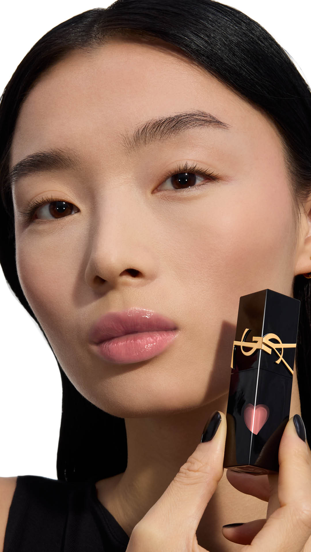 Modell mit hellem Hautton zeigt einen weichen, glänzenden Hellrosa-Lippenfarbton und hält die Flasche des YSL THE INKS VINYL CREAM Lip Stains neben ihre Wange.
