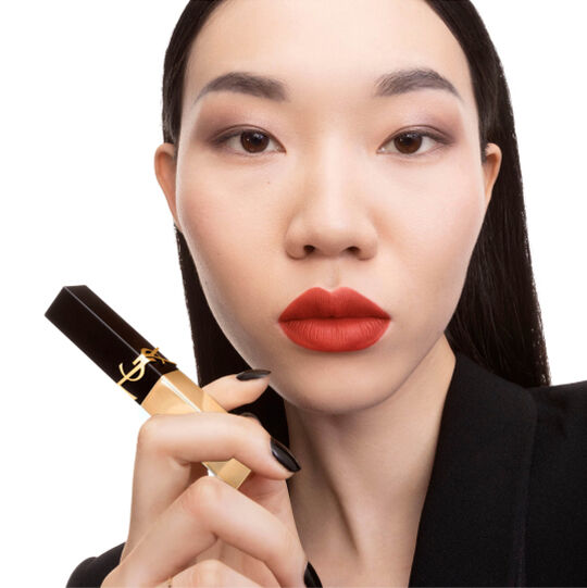 Hand mit schwarz-goldenem YSL Lippenstift mit quadratischer Spitze am Kinn.