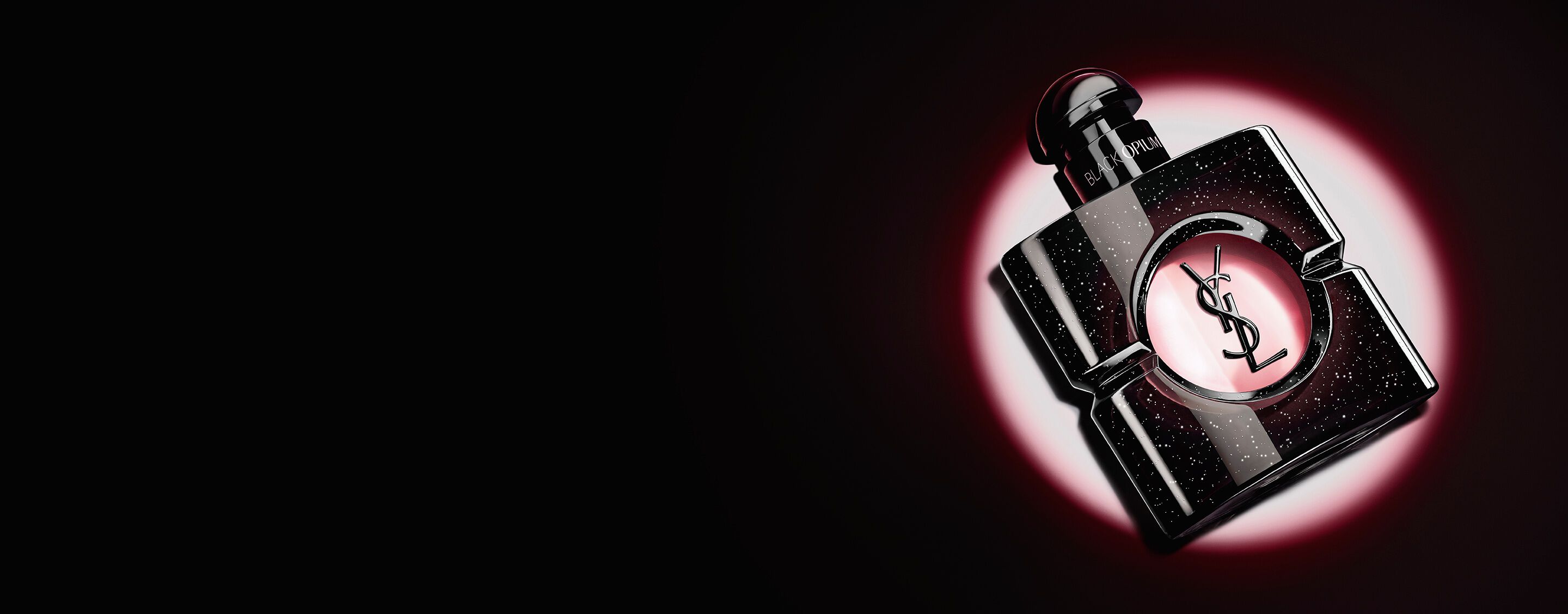 Black Opium Eau de Parfum Flakon, seitlich auf einer dunklen Oberfläche liegend, umgeben von einem rosa Lichtschein.