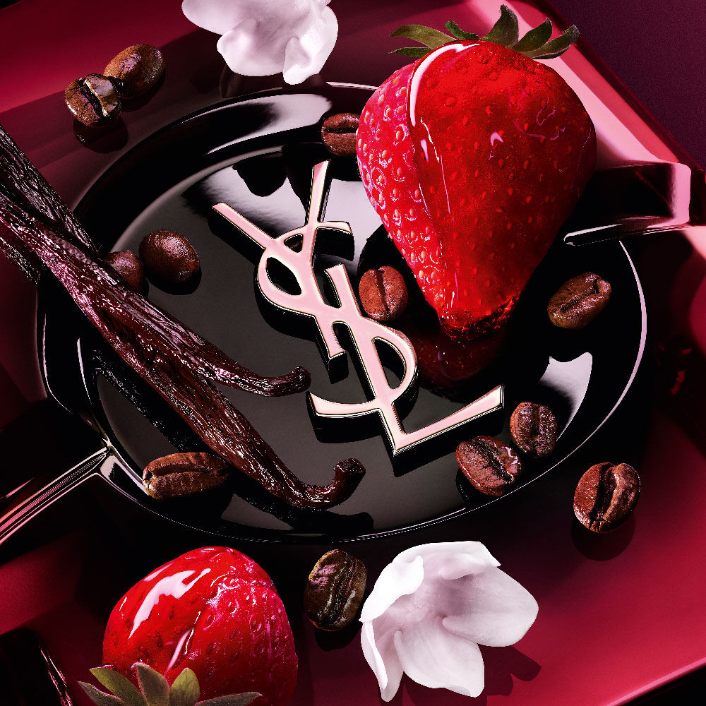 Nahaufnahme von frischen Erdbeeren, Vanilleschoten, Jasminblüten und gerösteten
                Kaffeebohnen, arrangiert um das Black Opium Eau de Parfum Pink Glaze Flakon mit dem
                ikonischen YSL Cassandre.