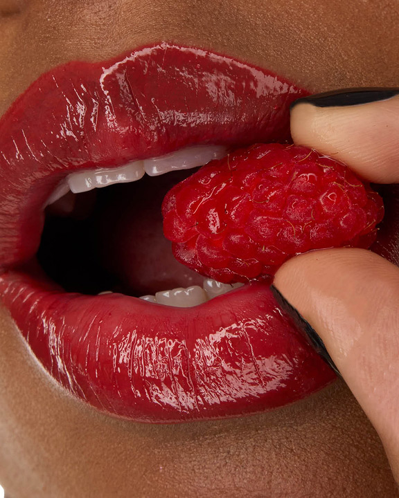 Nahaufnahme der Lippen von Model Zahara, geschminkt mit dem YSL LOVESHINE Lippenstift in der Nuance Berry Crush (Nr. 219), während sie eine frische Himbeere hält.