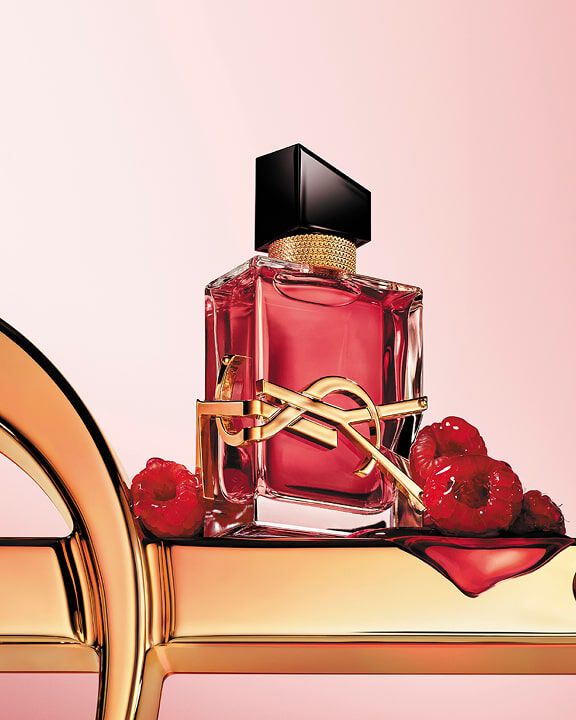 Roter YSL-Parfümflakon mit goldenem Logo auf einer goldenen Oberfläche mit Himbeeren.
